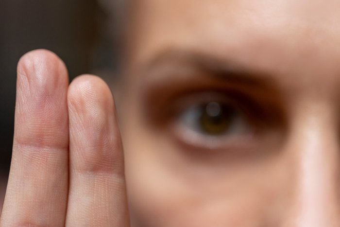 closely cropped shot of a woman holding up two fingers next to her face/eye - EMDR